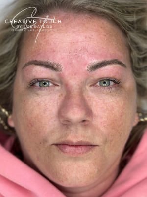 A close-up front view of a client's microbladed brows. More definition has been given, which in turn lifts her eyelid to open up her eyes. Shows off her beautiful green eyes. Slight redness around the treated area but that will go down within a few hours.