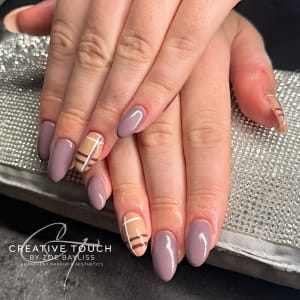 Close-up of hands with short, rounded oval nails. The design uses solid glossy mauve/dusty purple nails plus accent nails with a plaid/tartan pattern in beige, brown, and white lines on a light brown base.