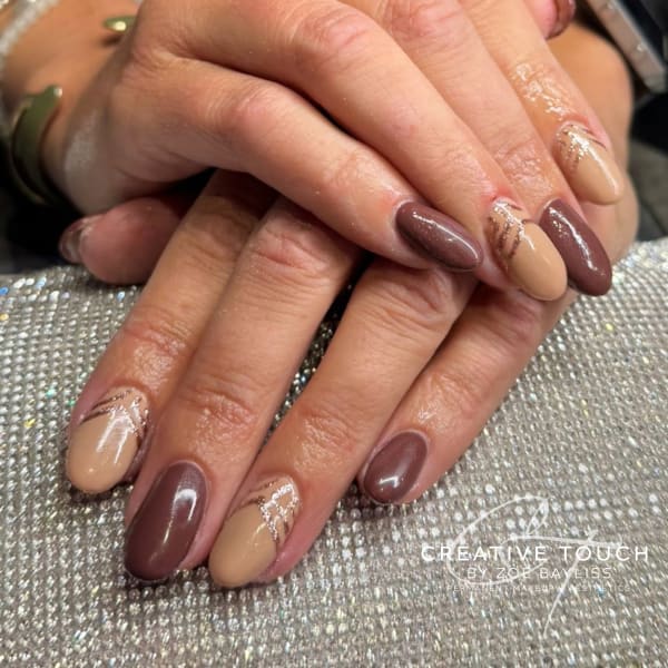 Close-up of hands with long, rounded oval nails. The design features an alternating pattern of solid, glossy deep mocha brown nails and solid light nude/beige nails. The nude accent nails are decorated with abstract, curved glittery silver/rose-gold stripes that mimic latte art.