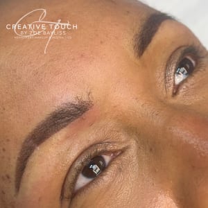 Fresh combination brows on medium-dark skin with warm undertones showing hair strokes and powder shading enhancing sparse natural brows with coordinated brown tones
