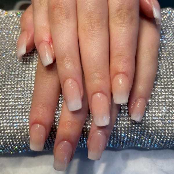 A clients hand after having BIAB builder in a bottle gel nails in an Ombr&eacute; finish. The nails are natural in colour and her hand rests on a diamond pillow.