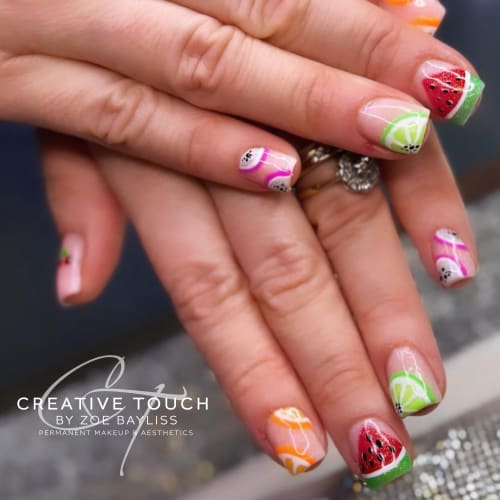 A close-up of the client's fingernails painted with a summer fruit theme of watermelon, lime, passionfruit, and orange slices against a nude basecoat