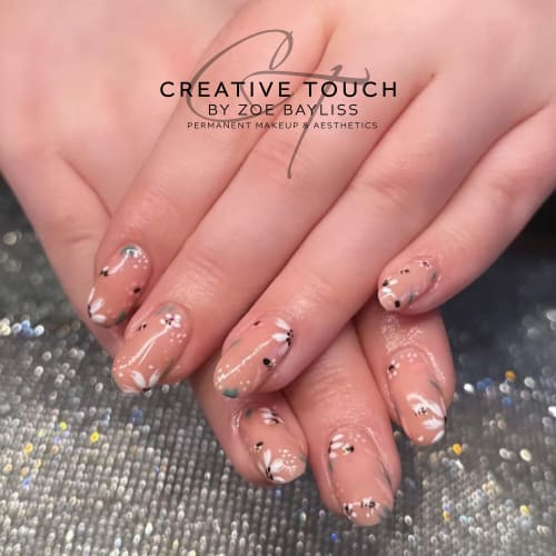 A close-up of a client's nails featuring a delicate floral design with soft black and white flowers and green accents
