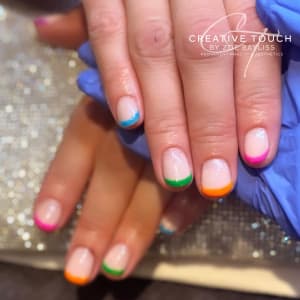 Close-up of client's nails with nail tips painted in mismatched vibrant colours: blue, green, orange and pink.