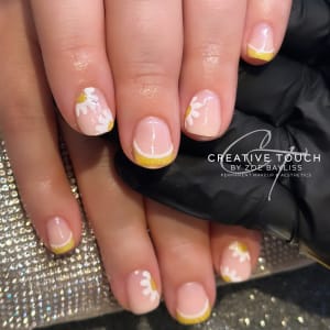 A close-up of a client's nails with hand-painted little daisies in soft white petals and sunny yellow centres.