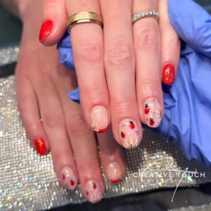 Close-up of a client's nails featuring a classic red base coat on the thumb and little finger, with tiny, detailed ladybugs hand-painted on each finger in between