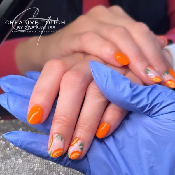 Close-up of a client's nails with a bright orange base coat on outer fingers and with hand-painted orange slices on middle fingers