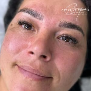 The client is lying on a couch with a white background. The client is looking away from the camera looking happy. The client has beautiful big brown eyes and lovely Mediterranean skin. The background is blurred while the focus is on the brows.