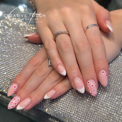 A close-up of hands with pink nails featuring a classic French tip design adorned with delicate pink daisies.