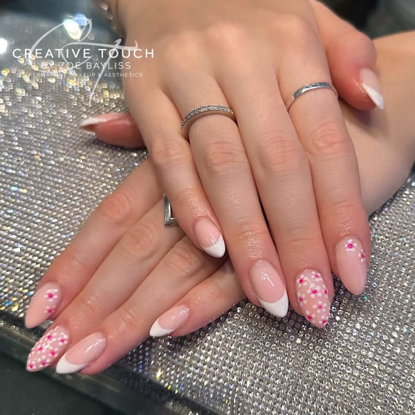 A close-up of hands with pink nails featuring a classic French tip design adorned with delicate pink daisies.