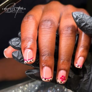 A close-up of hands with pink nails featuring leopard print tips and a single nail accented with a red flower.
