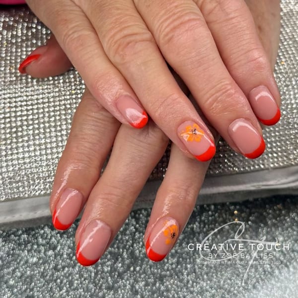 A close-up of hands with oval nails featuring a classic French tip in a vibrant blood orange colour, accented with a delicate orange flower on each hand.