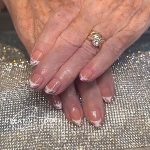 A close-up of hands with oval nails featuring a classic French tip design with two cherries and a green leaf on each tip.