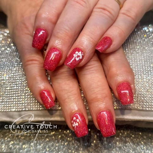 A close-up of hands with square nails featuring a deep red glitter basecoat with a single white floral design on each nail.