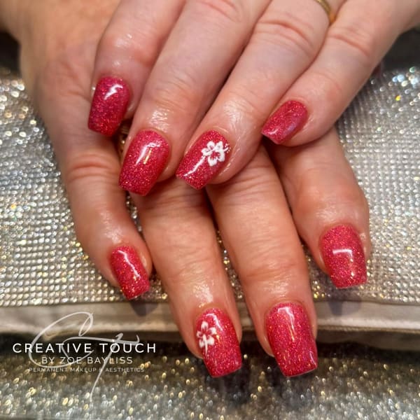 A close-up of hands with square nails featuring a deep red glitter basecoat with a single white floral design on each nail.
