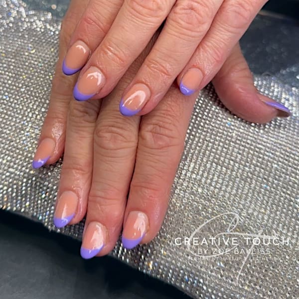 A close-up of hands with oval nails featuring a classic French tip design with a lavender-coloured tip.