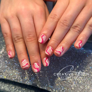 A close-up of hands with oval nails featuring a swirl design in shades of pink and white with glitter accents.