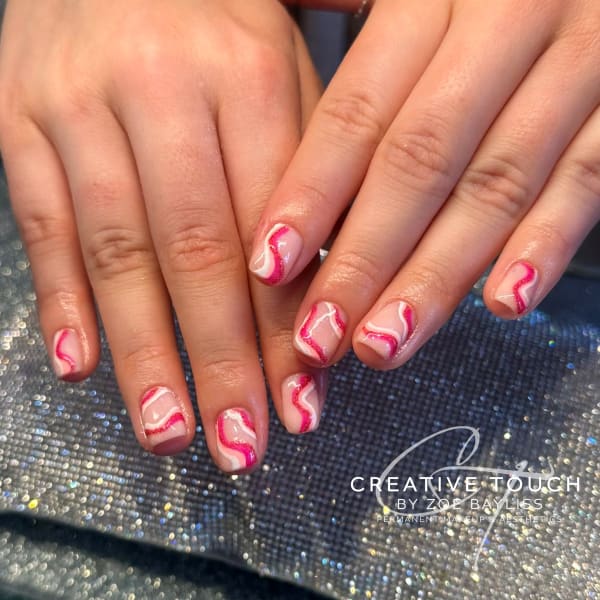 A close-up of hands with oval nails featuring a swirl design in shades of pink and white with glitter accents.