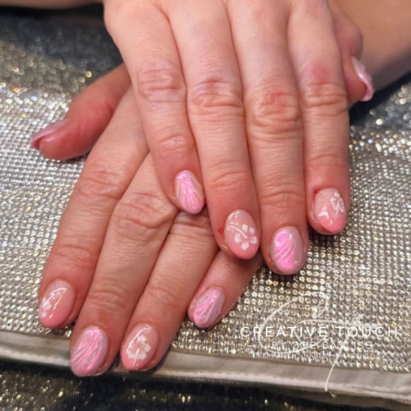 A close-up of hands with oval nails featuring a pink swirl design on a nude basecoat with white floral accents.