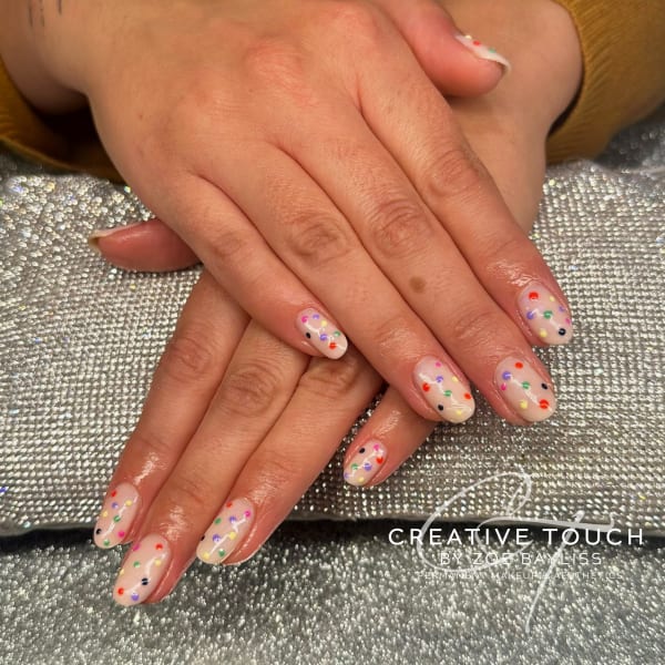 A close-up of hands with oval nails featuring a variety of colourful dots on each nail.