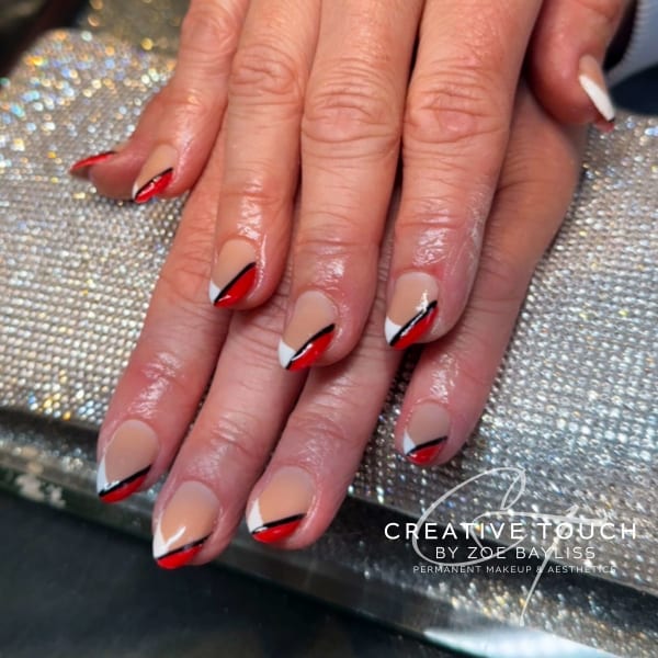 A close-up of hands with oval nails featuring a classic French tip design with a red and black geometric pattern on the tips.