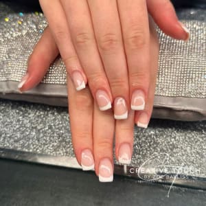 A close-up of hands with square nails featuring a classic French tip design with a white tip and a nude basecoat.