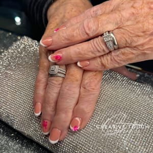 A close-up of hands with oval nails featuring a classic French tip design with delicate pink flowers on the first and ring fingers.