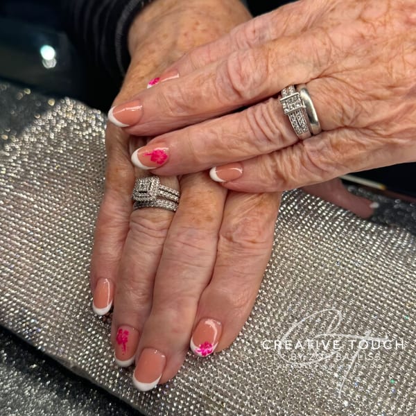 A close-up of hands with oval nails featuring a classic French tip design with delicate pink flowers on the first and ring fingers.