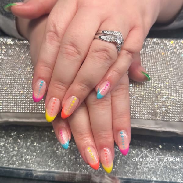A close-up of hands with oval nails featuring a bright colour design with pink, yellow, orange, and blue tips and matching coloured dots running down the length of each nail.