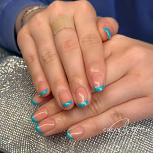 A close-up of hands with oval nails featuring a classic French tip design in a vibrant turquoise colour with a touch of glitter.