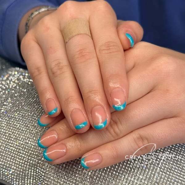 A close-up of hands with oval nails featuring a classic French tip design in a vibrant turquoise colour with a touch of glitter.