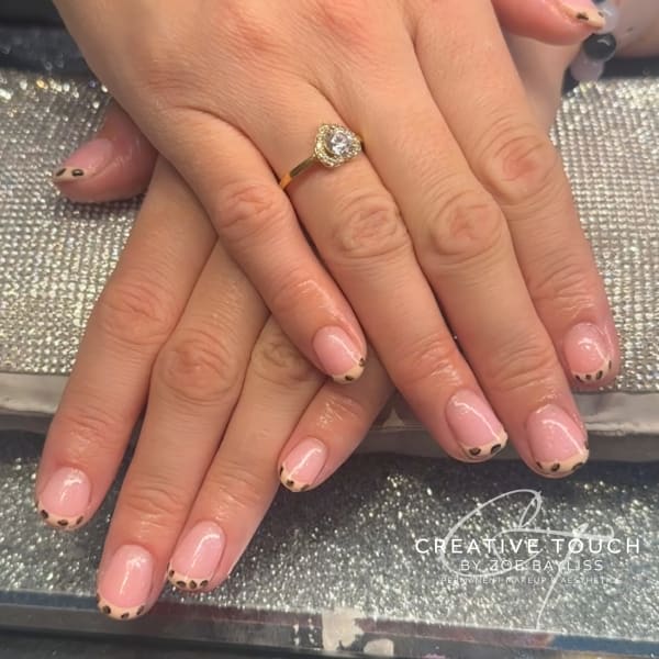 A close-up of hands with oval nails featuring a classic French tip design with subtle leopard spots on the tips.