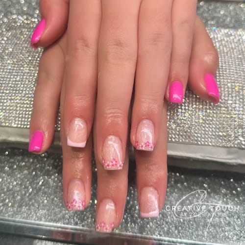 A close-up of hands featuring a pink French tip design, delicate pink flowers on the middle fingers and a mix of vibrant solid pink and nude base colours.