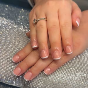A close-up of hands with short oval nails featuring a classic French tip design with a clean and minimalist aesthetic.