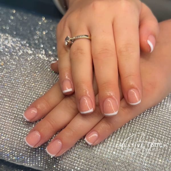 A close-up of hands with short oval nails featuring a classic French tip design with a clean and minimalist aesthetic.