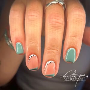 A close-up of hands with oval nails featuring a pastel green base coat on first and little fingers, a peach-toned base of each nail on the middle fingers, and white half moon with polka dots on the peach section.