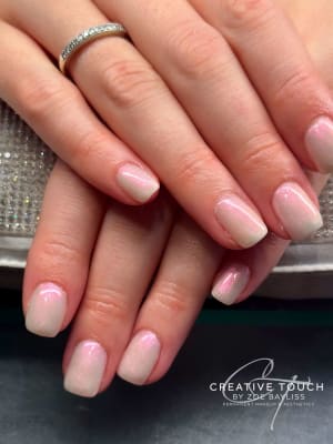 A close-up of hands with oval nails featuring a soft pink base coat with a pearlescent shimmer finish.