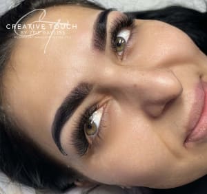 Our client is smiling, looking away from the camera. The client is of dark complexion, hence her choosing a darker shade for her eyebrows. Her brows are well-shaped and her bulb is fashioned of a fade-out. The client has locker green eyes which compliments the dark tint. She also had her lashes done at the same time with Grace.