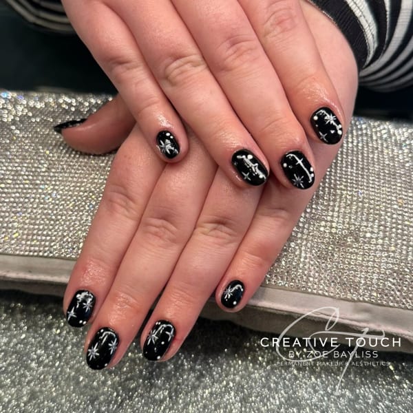 A close-up of hands with oval nails painted black, adorned with silver star accents.