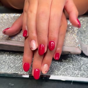 A close-up of hands with oval nails painted a vibrant cherry red, with a single cherry motif on the ring finger.