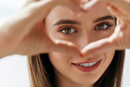 Woman framing her face with hands in heart shape, demonstrating self-care and appreciation for natural skin health
