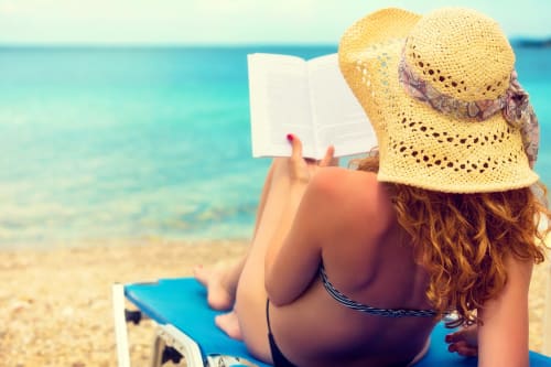 Woman relaxing at the beach, laying on a sunbed and reading a book