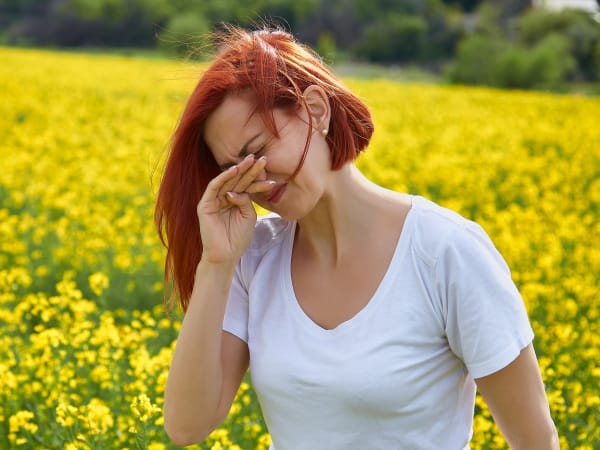 A woman with a pollen allergy standing in a field of flowers sneezing