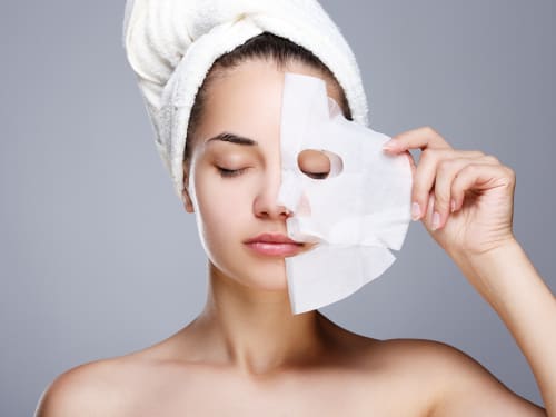 A young woman peeling off a facial mask to reveal beautiful, youthful skin