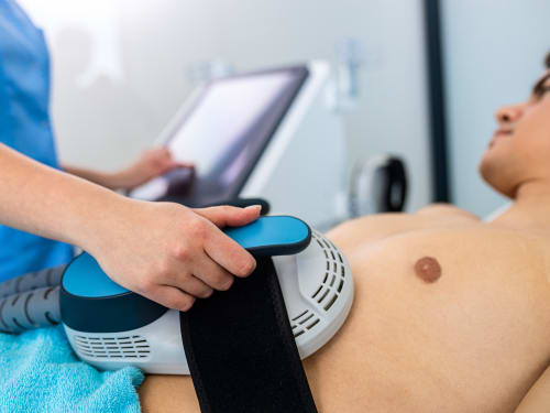 A beautician applying HIEMT paddles to the abdominal muscles of a young man