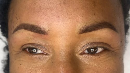 Fresh ombr&eacute; powder brows on dark skin showing symmetrical defined arches with natural gradient effect and medium brown pigment coordination