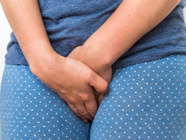 A woman suffering incontinence from pelvic floor weakness clutches her crutch in discomfort