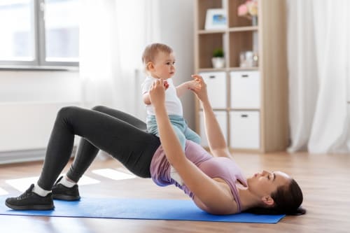 A young mother with her baby, exercising at home to build pelvic floor strength