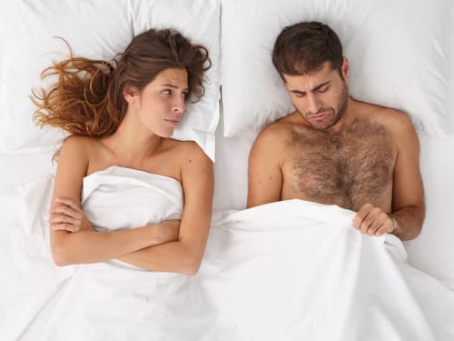 A couple in bed showing signs of frustration caused by intimacy issues
