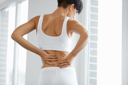 A woman holding her lower back in pain as she looks out of a window